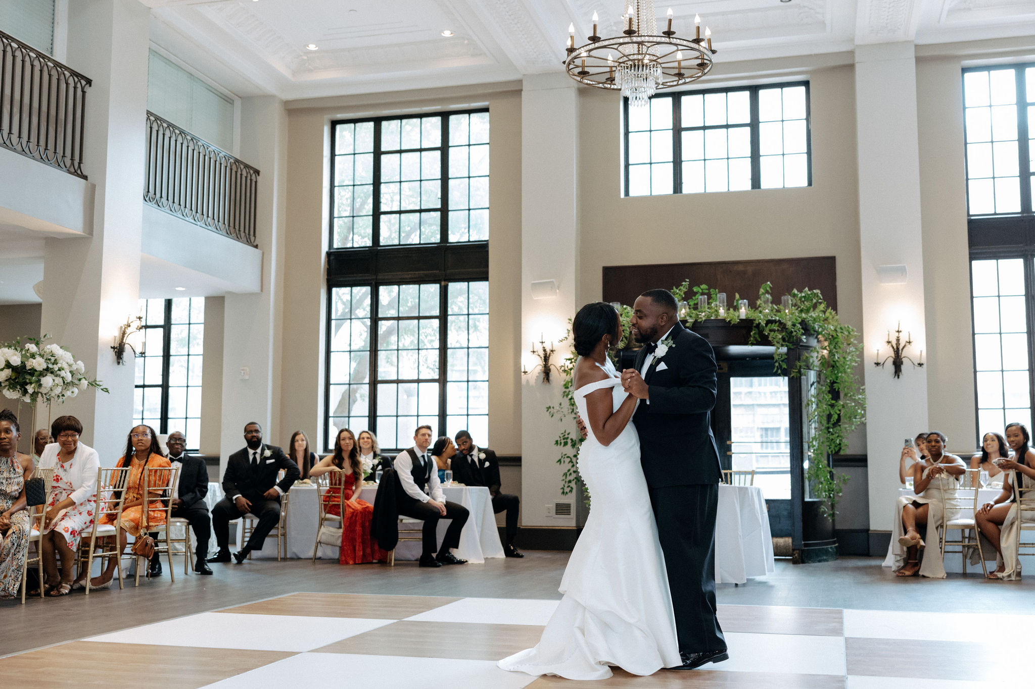 A bride and groom have their first dance on a checkered floor at 1208 Washington Place in Columbia, SC. Their family and friends surround them at tables around the perimeter of the room.