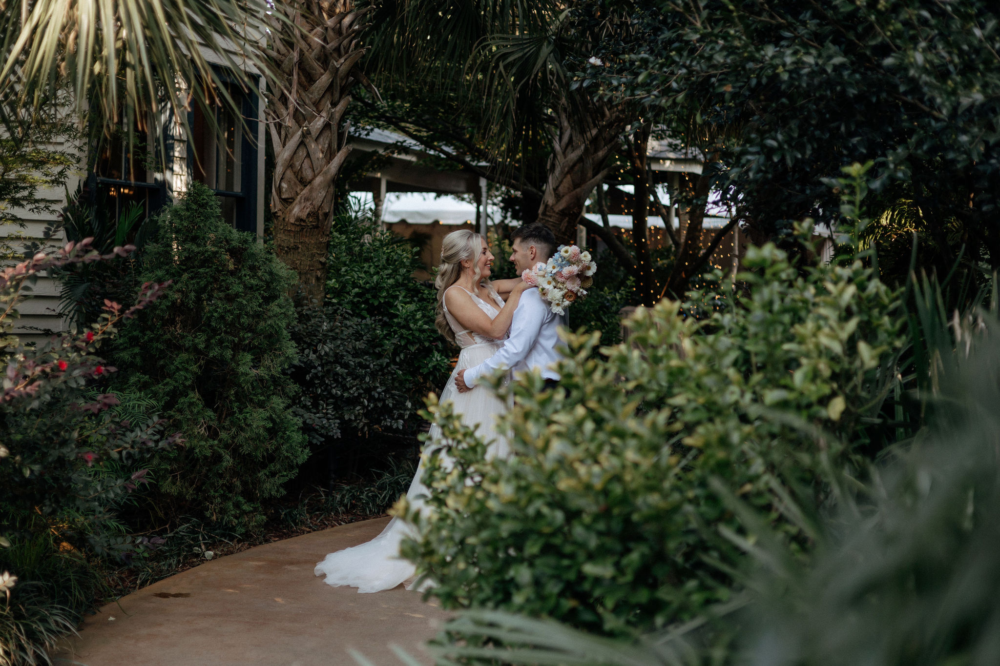 A bride and groom face each other and smile hidden in a garden at the River Road and Jasmine House in Columbia, SC.