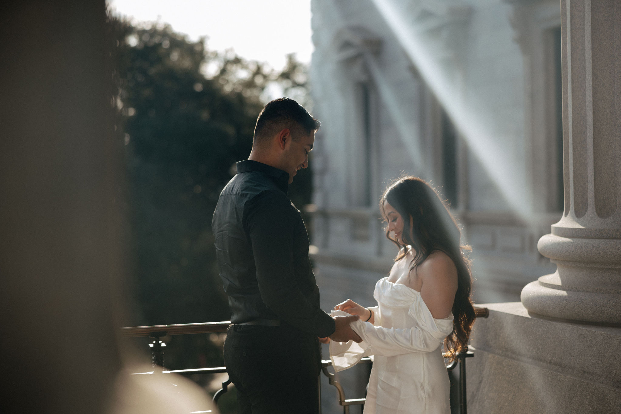 A couple stands facing each other at the top of the SC State House during golden hour. They hold each others hands.