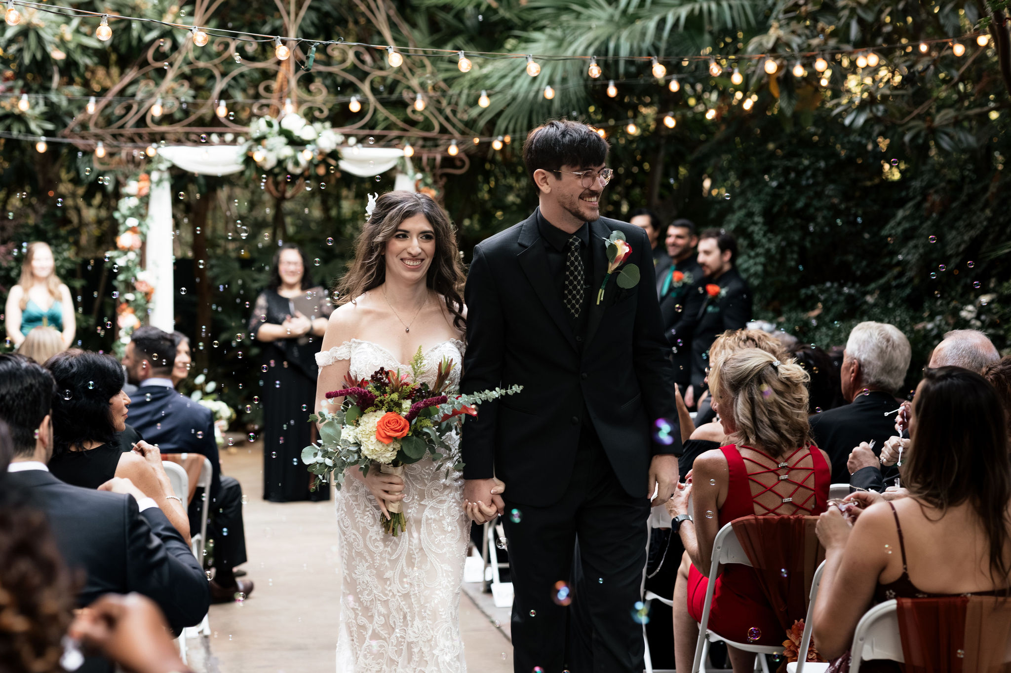 A couple walks back down the aisle after their wedding ceremony holding hands and smiling at their guests at the River Road and Jasmine House and Gardens in Columbia, SC.