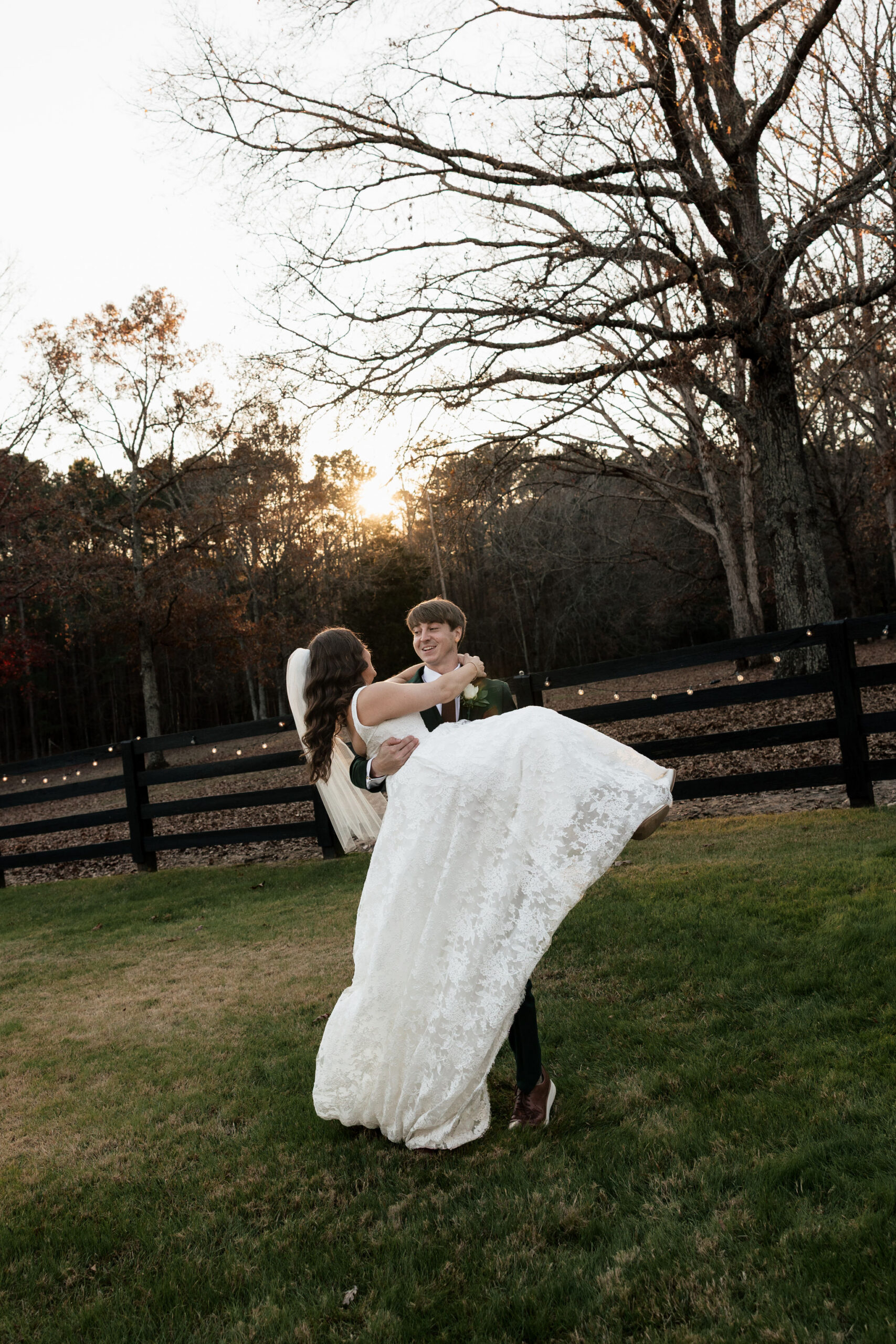 A groom picks up his bride and spins her around during golden hour on their wedding day at Oakbrook Farm in Ridgeway, South Carolina.