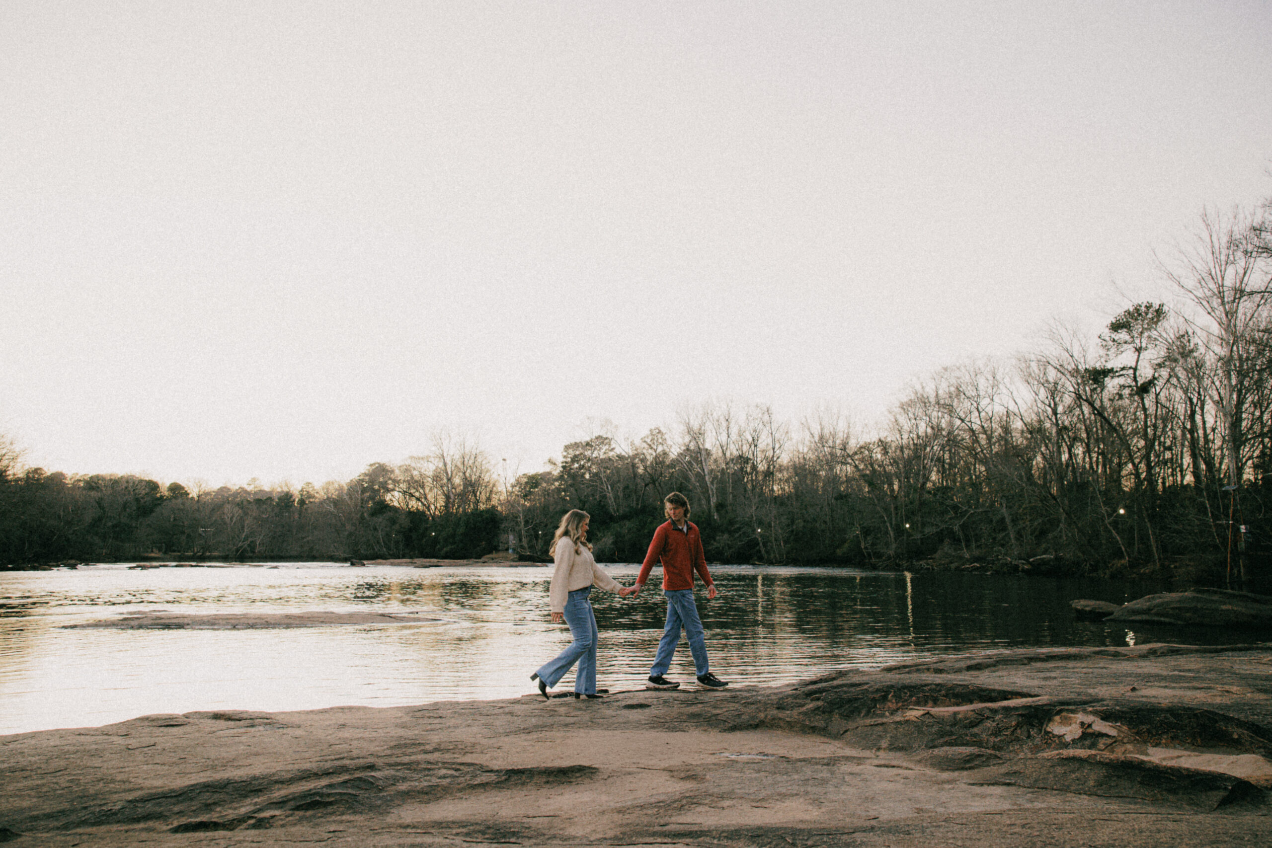 Devon and Elissa hold hands during their engagement session as they walk along a large rock at the Saluda Riverwalk in Columbia, SC.